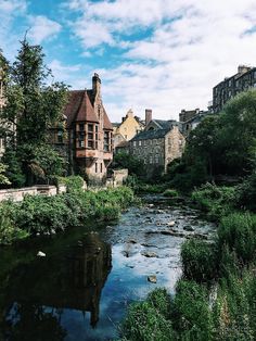 a river running through a lush green park next to tall buildings on the side of a road