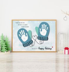 two blue mittens with happy holidays written on them are next to a christmas tree