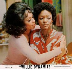 two women embracing each other in front of a store sign that says, willie dynamite