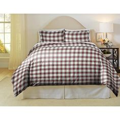 a bed with a plaid comforter and pillows on top of it in front of a window