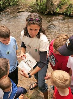 a group of young children standing next to each other in front of a river holding papers