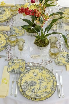 the table is set with yellow and blue plates, silverware, and flowers in glass vases