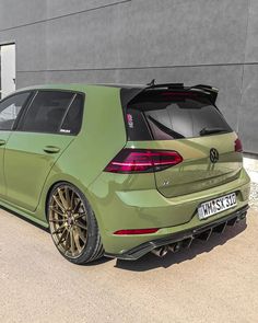 the rear end of a green car parked in front of a gray building with its trunk open