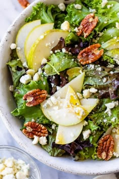 a salad with apples, pears and feta cheese in a white bowl on a marble table