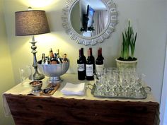 a table topped with lots of bottles of wine next to a lamp and a mirror