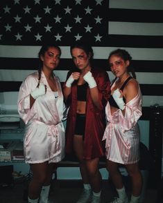 three women in white robes posing for a photo with an american flag on the wall behind them