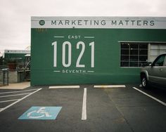 an empty parking lot with a green sign on the wall and a car parked in front of it