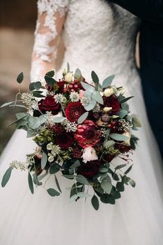 a bride and groom holding a bouquet of red roses, greenery and white blooms