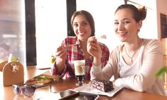 two women sitting at a table eating cake and drinking milk