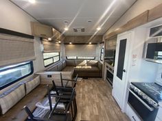 the interior of an rv with wood flooring and couches, windows, and cabinets