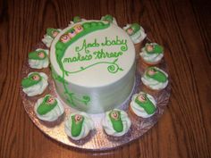 a birthday cake decorated with green and white icing on a wooden table next to cupcakes