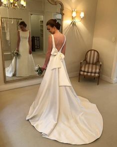 a woman standing in front of a mirror wearing a white dress with a bow on the back