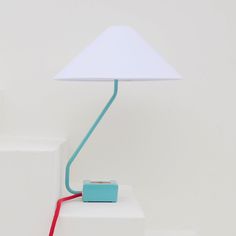 a blue and red lamp sitting on top of a white table next to a wall