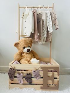 a teddy bear sitting in a wooden crate with clothes hanging on the wall behind it