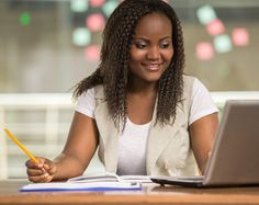 a woman sitting at a desk with a laptop and notebook in front of her, smiling