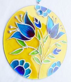 a yellow plate with blue flowers and green leaves on the side, hanging from a chain