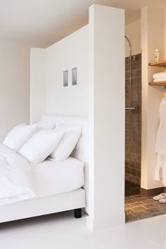 a bed with white sheets and pillows in a room next to a shower stall on the wall