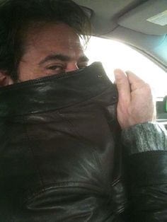 a man is sitting in the back seat of a car and covering his face with a leather jacket