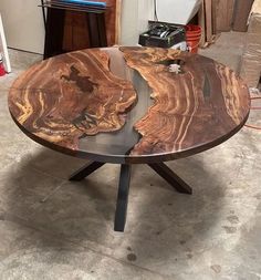 a table made out of wood and metal with a black base in the middle, sitting on concrete flooring