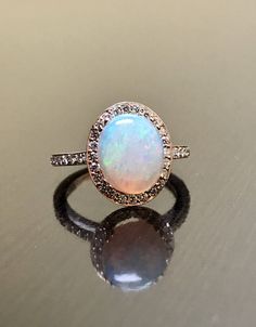 DeKara Designs Collection Our latest design! An elegant and lustrous Opal cabochon surrounded by beautiful diamonds in a halo setting. Metal- 14K Rose Gold, .583. Size- 4-12 Stones- Center Features a Oval Fiery Opal Cabochon Cut 2.60-2.90 Carats, 11.10 MM Long, 9 MM Wide, 44 Round Diamonds, F Color VVS Clarity, 0.35 Carats. Latest of my creations. A beautiful Opal Halo Diamond Ring. The Opal is professionally prong set in between 4 double prongs. There are 10 pave set round diamonds on each side Luxury Rose Gold Opal Gemstone Ring, Formal Rose Gold Opal Ring With Diamond, Luxury Rose Gold Opal Ring, Elegant Opal Jewelry With Halo Setting, Elegant Cabochon Opal Ring For Wedding, Formal Rose Gold Cabochon Ring, Elegant Opal Ring With Halo Setting In Diamond White, Elegant Opal Ring With Diamond In Rose Gold, Elegant Opal Promise Ring With Cabochon