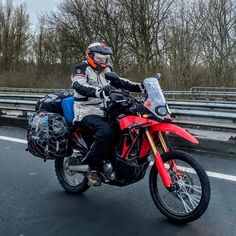 a man riding on the back of a red motorcycle down a street next to a highway