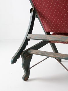 an old wooden chair with red fabric on it's back and armrests