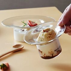 someone is scooping some ice cream out of a glass cup with strawberries on the side