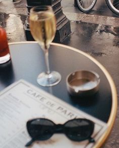 a glass of wine sitting on top of a table next to a newspaper and some glasses