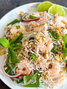 a white plate topped with shrimp and veggies on top of a table next to a lime wedge