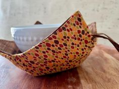 an orange and brown fabric bird sitting on top of a wooden table next to a white bowl