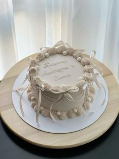 a white cake sitting on top of a wooden table covered in icing and ribbons