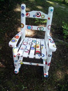 a white wooden rocking chair with circles painted on it's back and sides, sitting in the grass