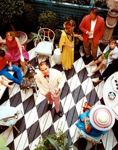 a group of people sitting around tables and chairs in an outdoor area with black and white checkered flooring