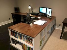 a computer desk with two monitors and bookshelves on top of it in an office