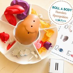 an egg in a cup surrounded by other toys on a plate with roll a body number recognition game