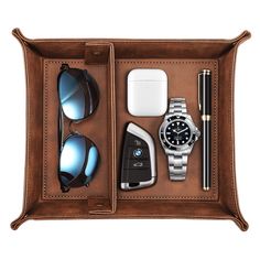 an open leather case with sunglasses, watch and other items in it on a white background