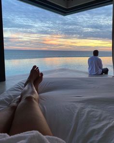 a man sitting on top of a bed next to a window looking out at the ocean