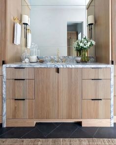 a bathroom vanity with marble counter top and wooden cabinetry, along with two vases filled with flowers