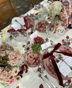 the table is set with red and white china plates, silverware, and flowers