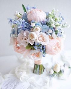 a bouquet of pink and blue flowers on a white table with a book in the background