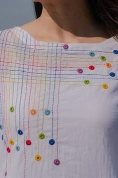 a woman wearing a white top with colorful buttons on it's chest and neck