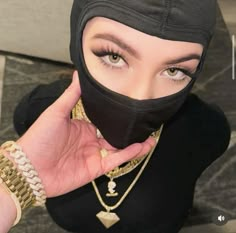 a woman wearing a black head covering holding her hand up to her face with gold chains around her neck