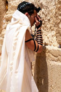 a man dressed in white talking on a cell phone while standing next to a stone wall