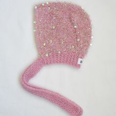 a pink knitted hat with sequins on the brim is laying on a white surface