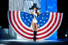 a woman is walking down the runway with an american flag cape on her head and boots