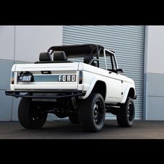 a white ford bronco truck parked in front of a garage door with it's hood up