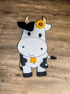 a paper cow with a sunflower on it's head sitting on a wooden floor