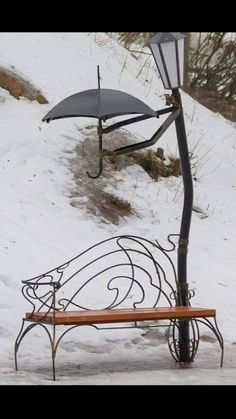 a bench with an umbrella attached to it sitting in the snow next to a lamp post