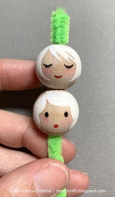 two little dolls with green hair are sitting on top of each other's fingers