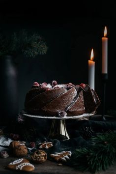 a chocolate cake with icing and cranberries sits on a table next to two lit candles